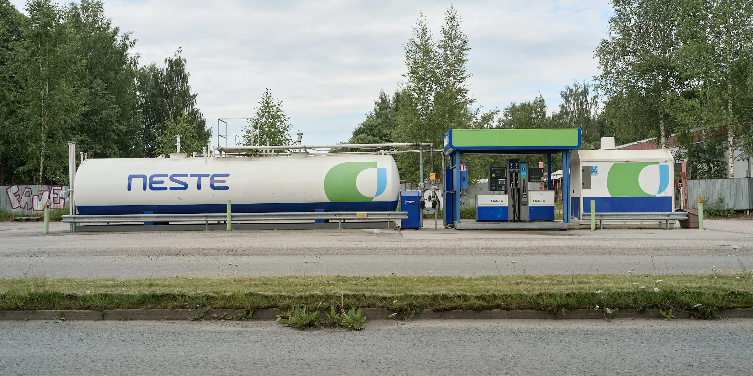 Kleine Tankstelle mit weißem Tank vor grüner Baumkulisse