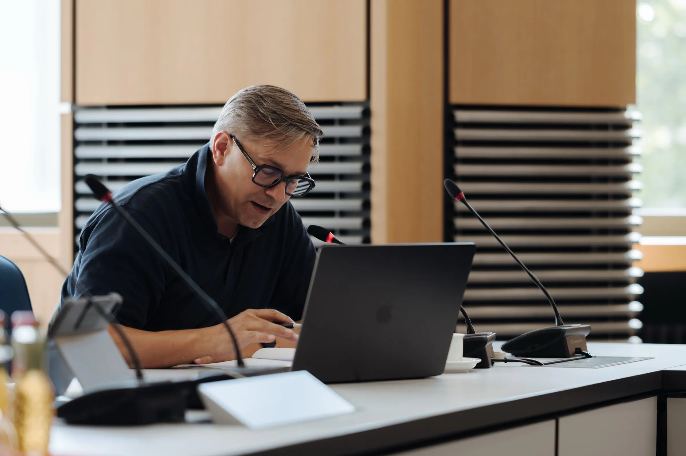 Roman Thomas arbeitet am Laptop am Sitzungstisch, vor ihm Mikrofone