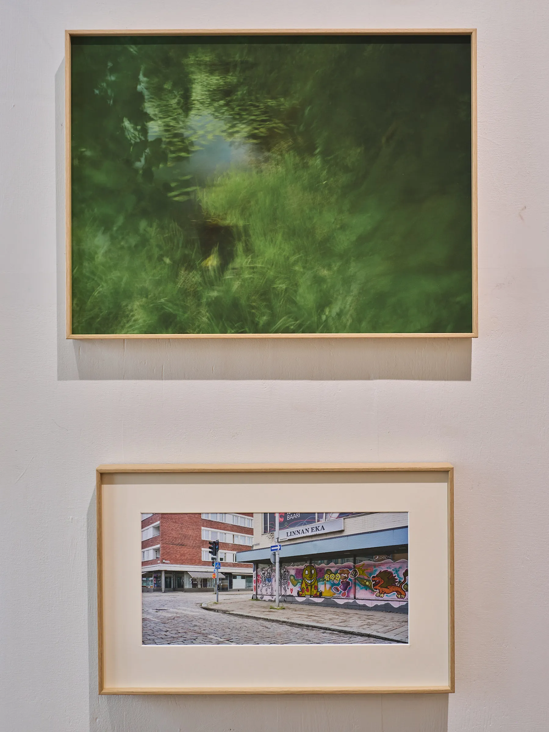 Zwei gerahmte Fotografien übereinander, oben ein grünes Wasserbild, darunter eine Straßenecke mit Graffiti