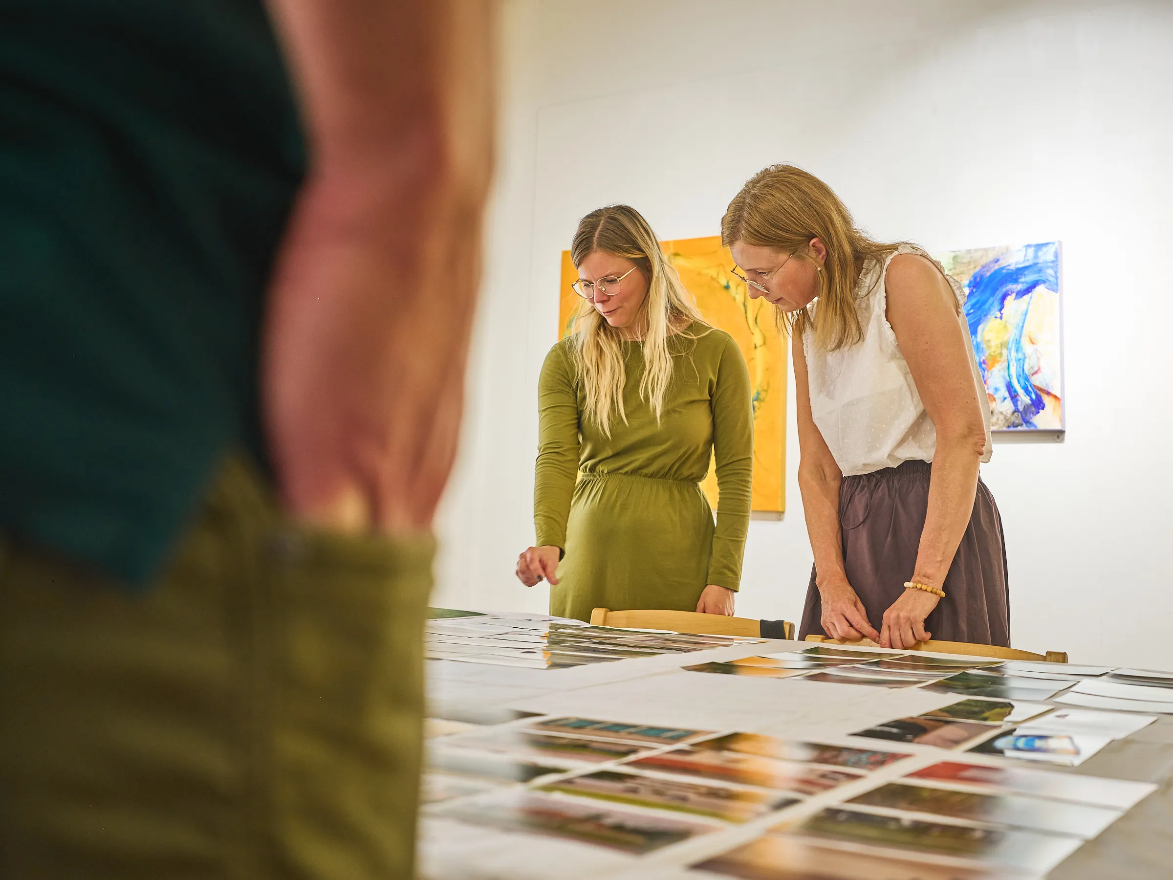 Zwei Frauen beugen sich über die ausgelegten Fotografien und schauen sie an