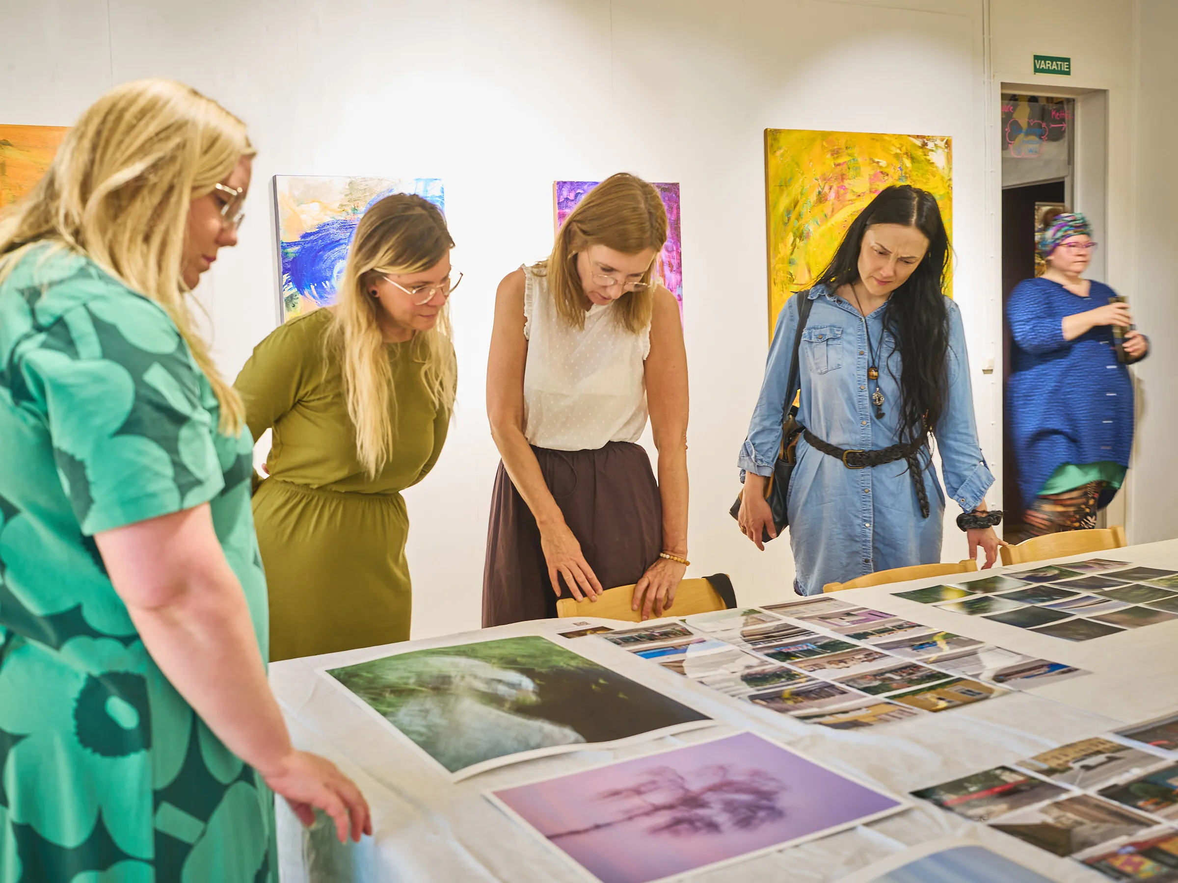 Gruppe von Frauen am Tisch mit den Bildern, vorn ein grün gemustertes Kleid