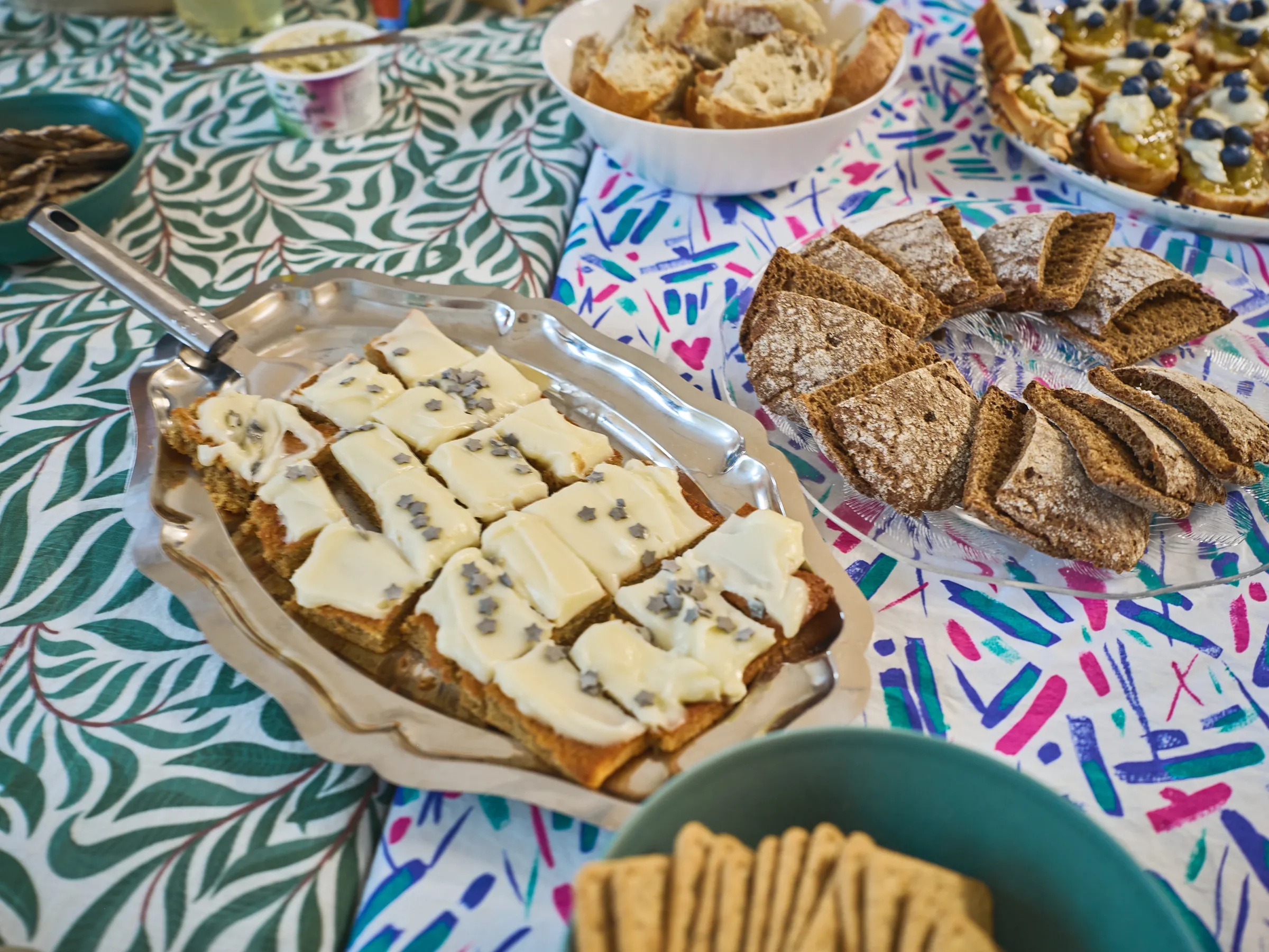 Platten mit hellem und dunklem Brot, belegten Stücken und einem Korb mit Knäckebrot auf gemustertem Tuch