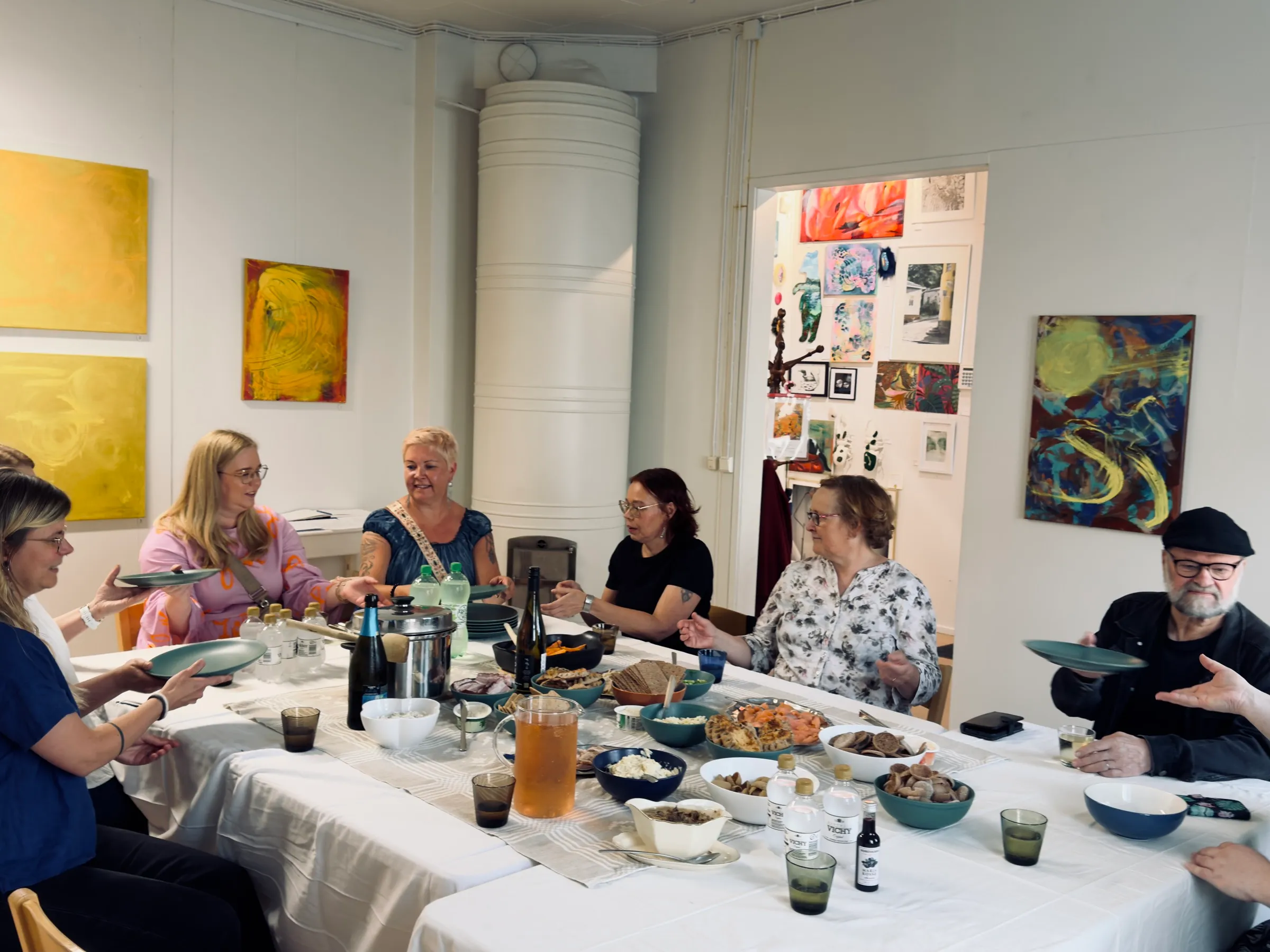 Gemeinsames Essen an einer langen Tafel im Galerieraum des Kulttuurikonttori, an den Wänden Malerei