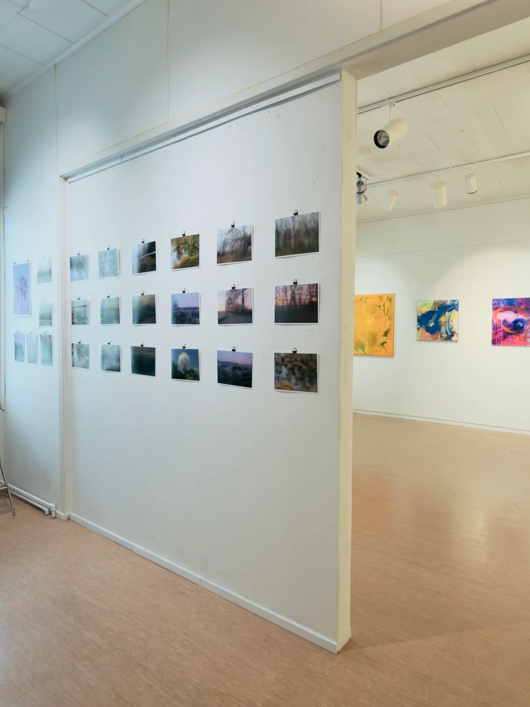 Blick durch einen Ausstellungsraum bei Kaputa ry, im Vordergrund gehängte Fotoabzüge, im Hintergrund abstrakte Gemälde