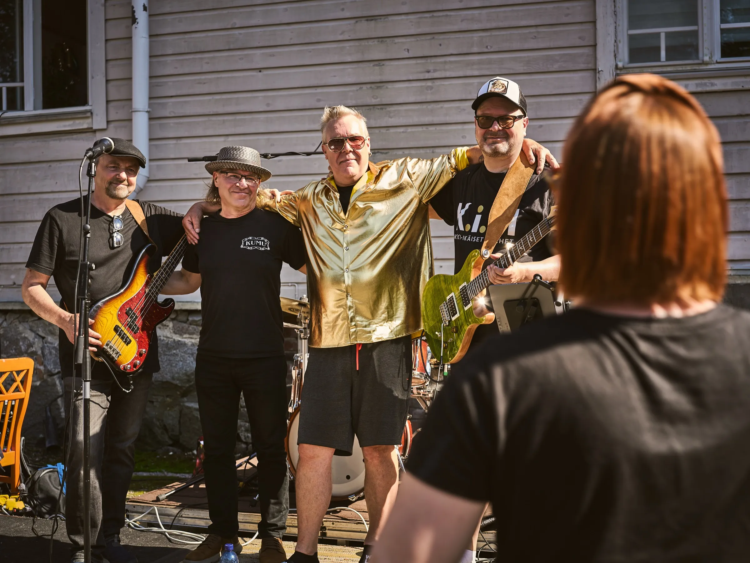 Vier Musiker der Band stehen Arm in Arm vor dem Holzhaus und lassen sich fotografieren