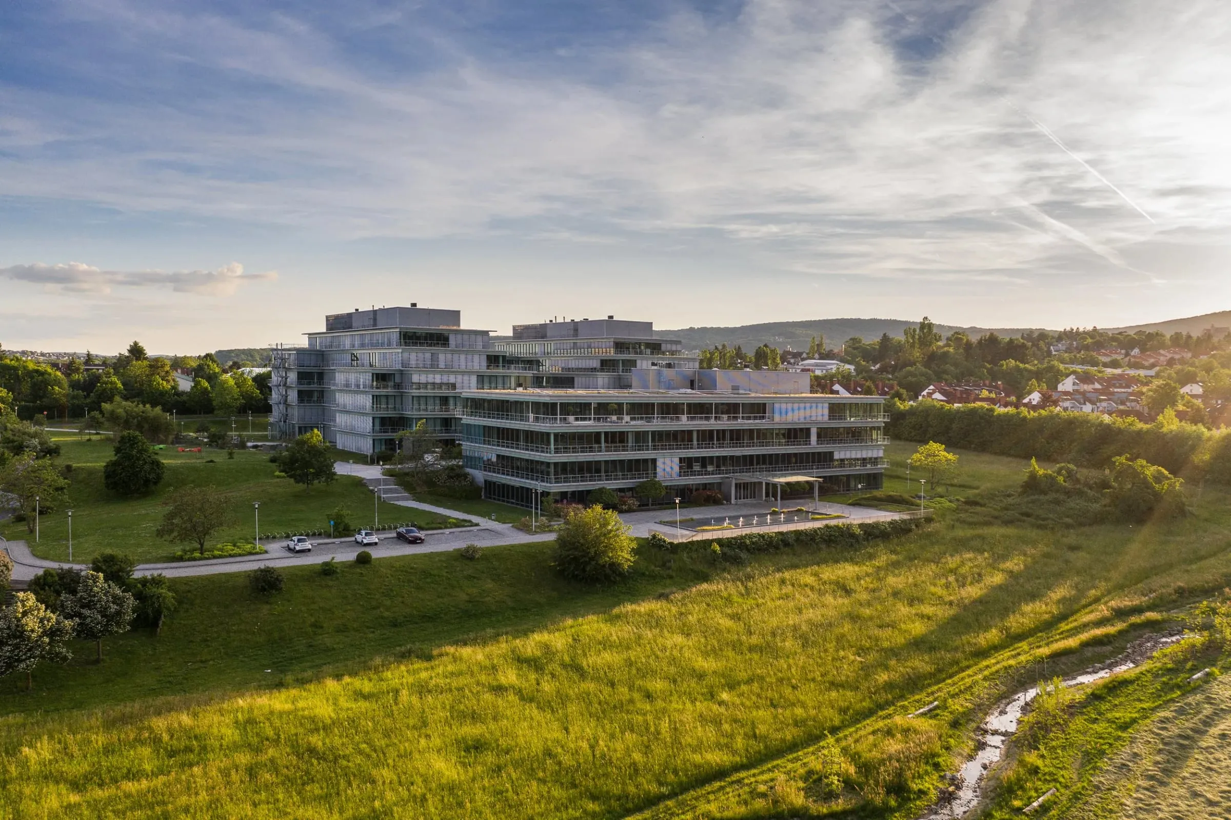 Luftaufnahme des Accenture Campus bei Frankfurt im Abendlicht, gläserne Bürogebäude zwischen grünen Wiesen und Hügeln