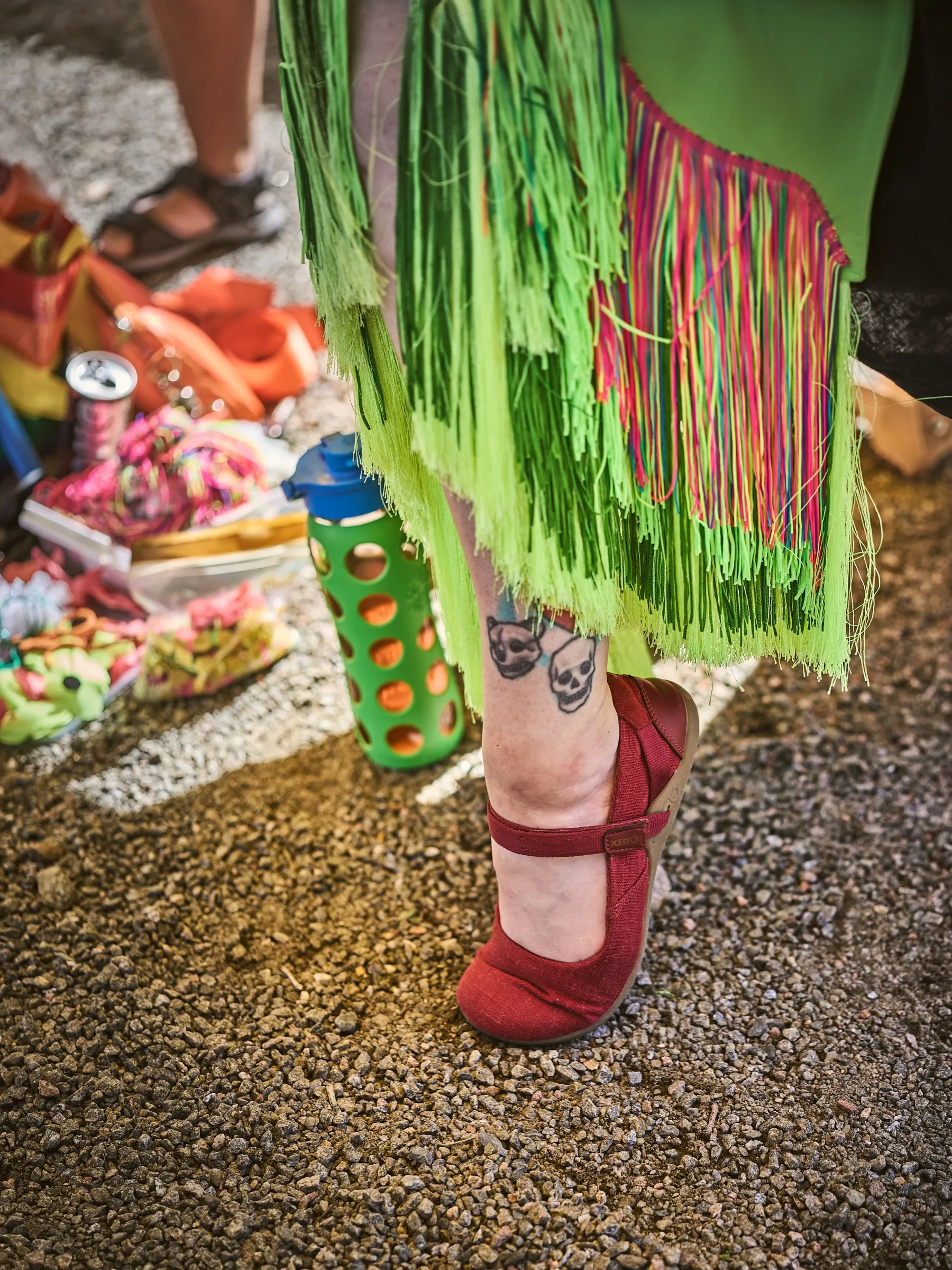 Detail eines bunten Fransenkostüms und roter Schuhe auf Kies beim Sommerfest