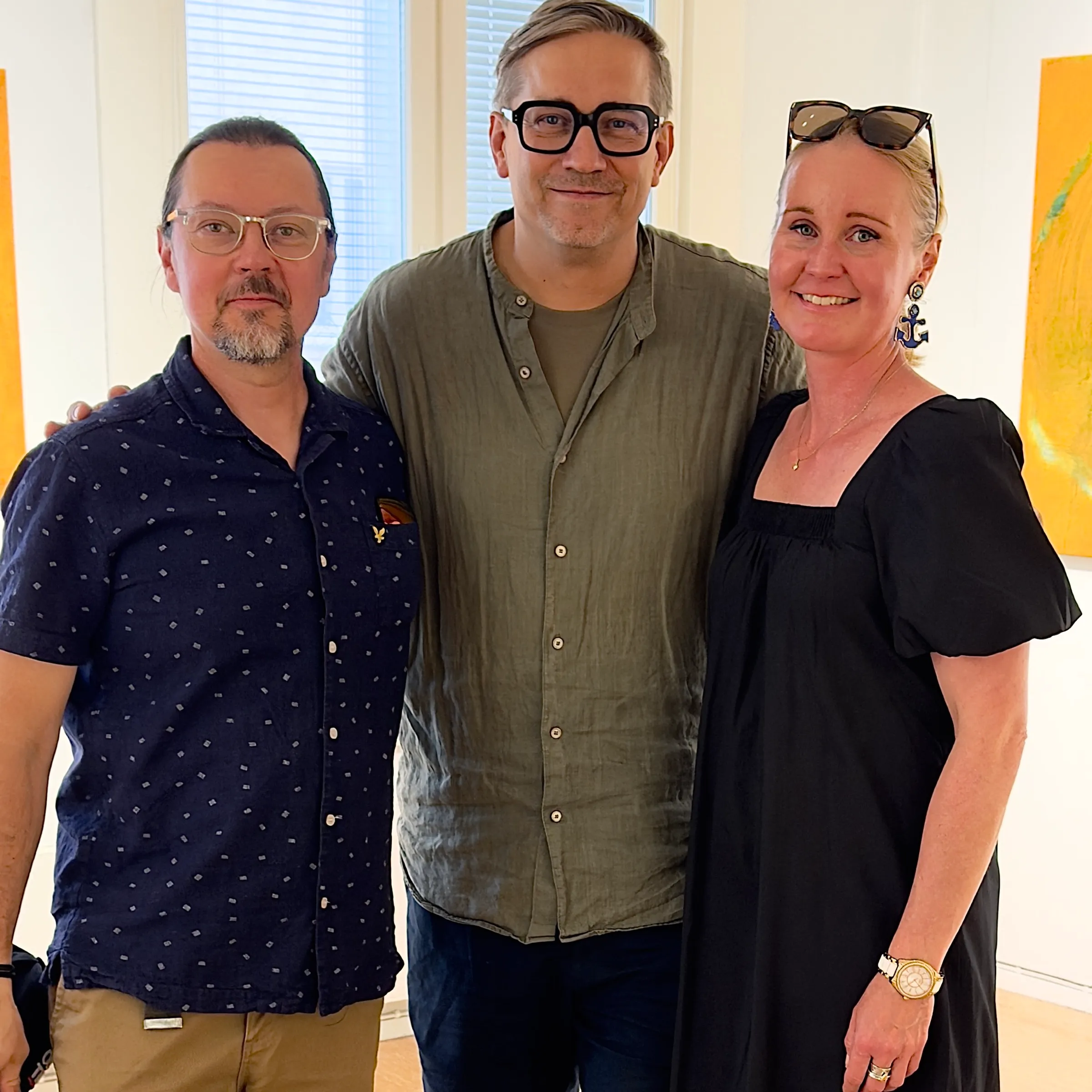Sami, Roman und Kathri stehen lächelnd nebeneinander in einem hellen Galerieraum, Hochformat