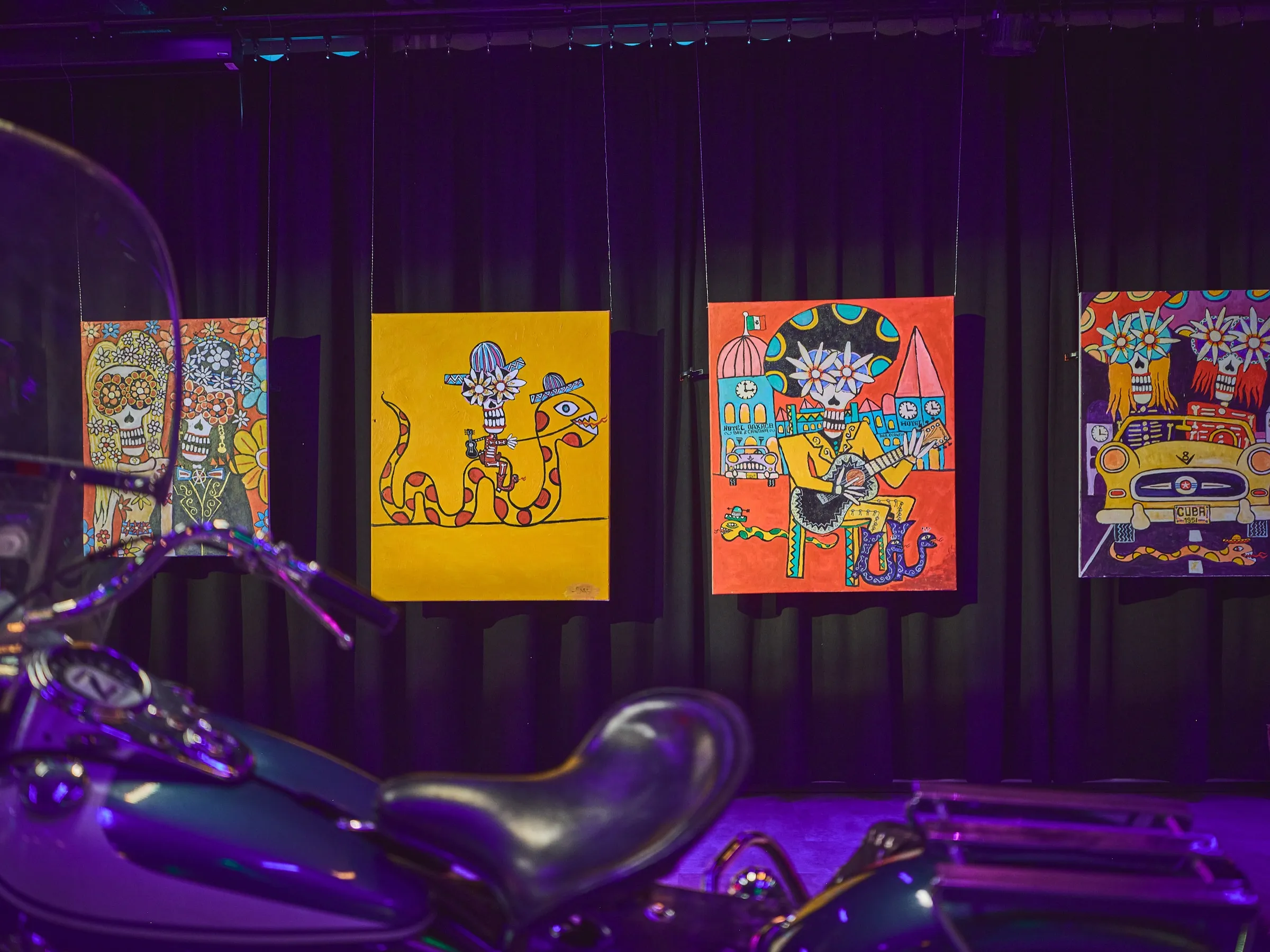 Dunkler Chopper im Vordergrund, dahinter kleine bunte Bilder an der Wand