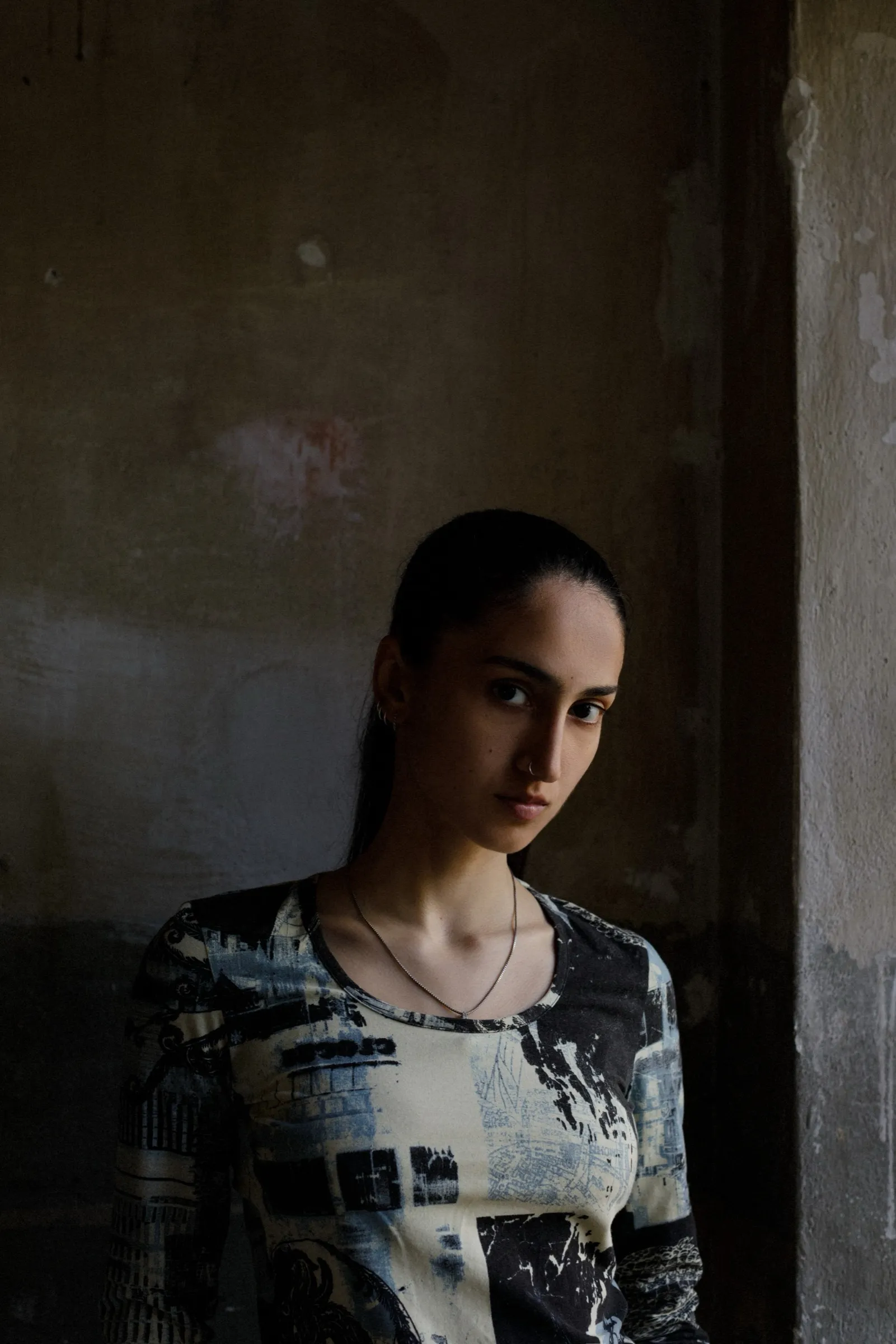 Porträt von Leyla Yenirce, sie lehnt an einer rauen, fleckigen Wand und schaut seitlich in die Kamera