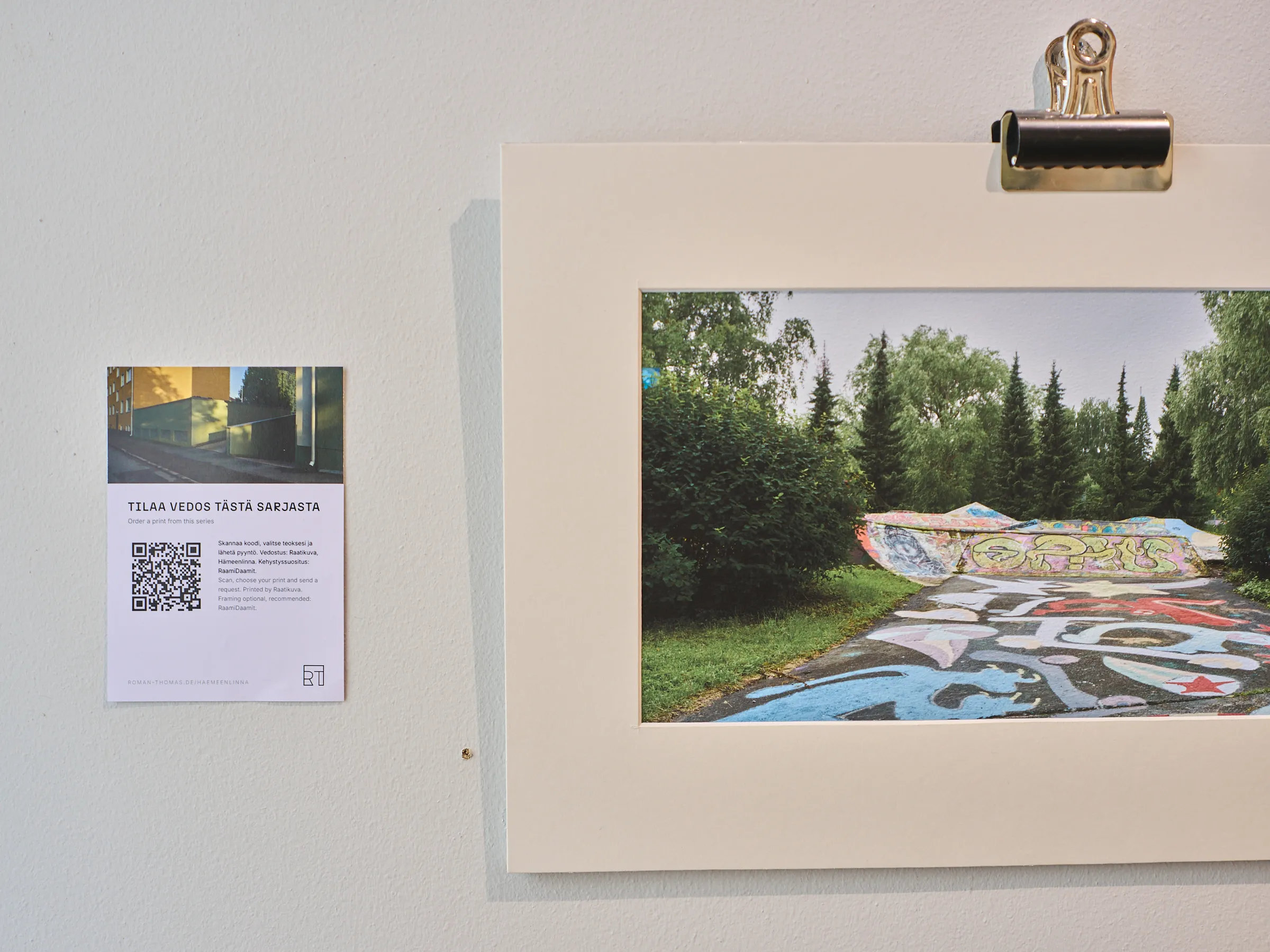 Weiße Infotafel mit finnischem Text und QR-Code neben einer geklammerten Fotografie eines bemalten Skateparks