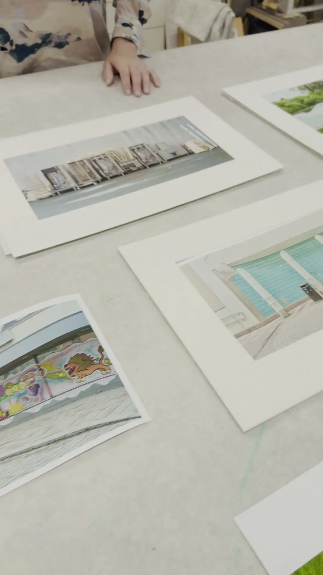 Video: Blick über den Werkstatttisch mit ausgelegten Prints, im Hintergrund wird gearbeitet