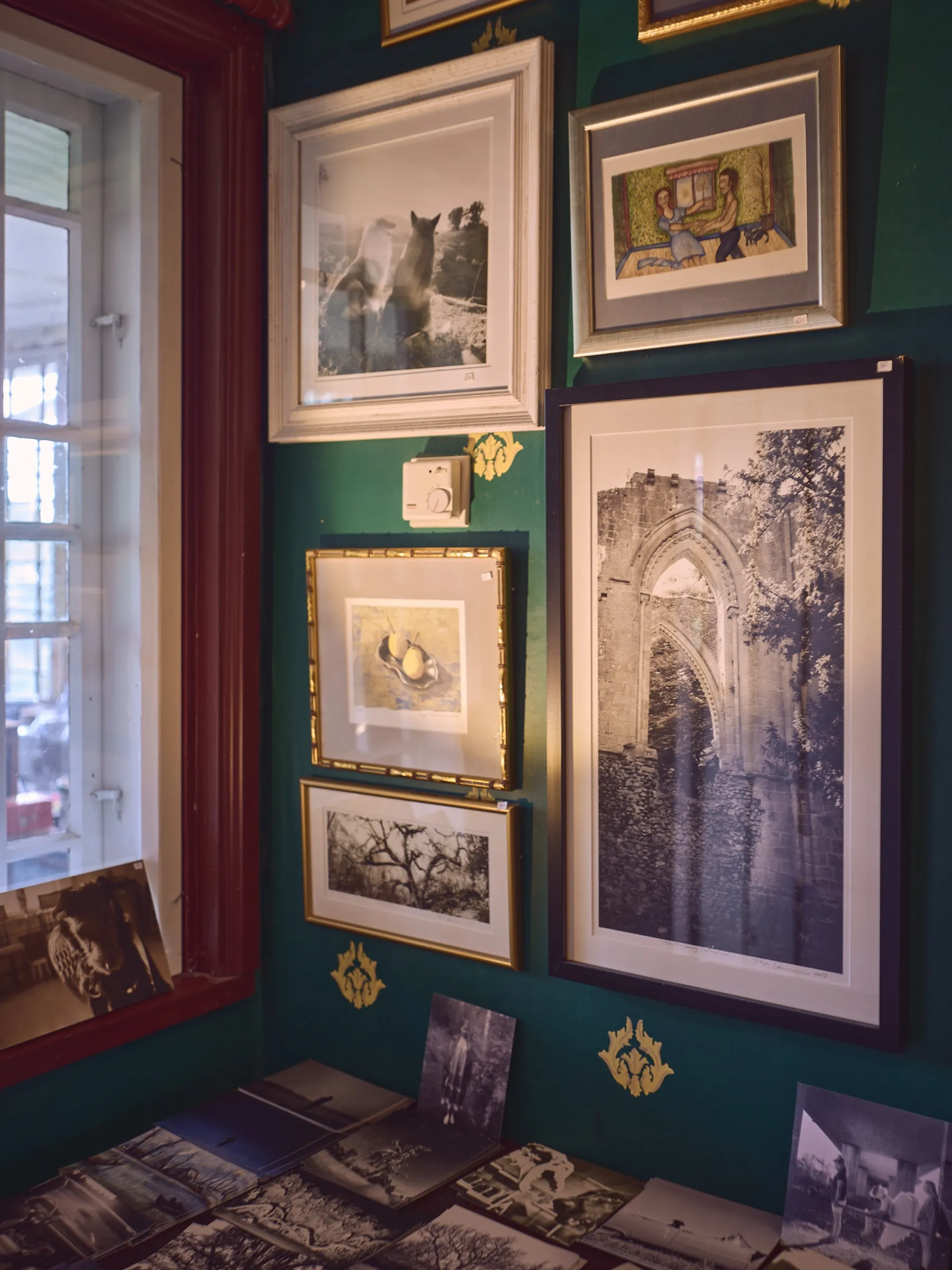 Grüne Wand dicht behängt mit gerahmten Fotografien und Grafiken, Hochformat