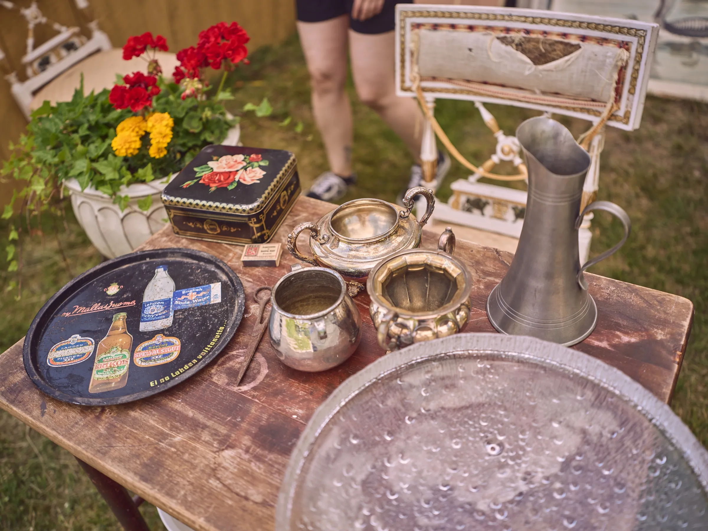 Flohmarkttisch mit Silberkannen, Tabletts, Blumen und einer großen Glasplatte