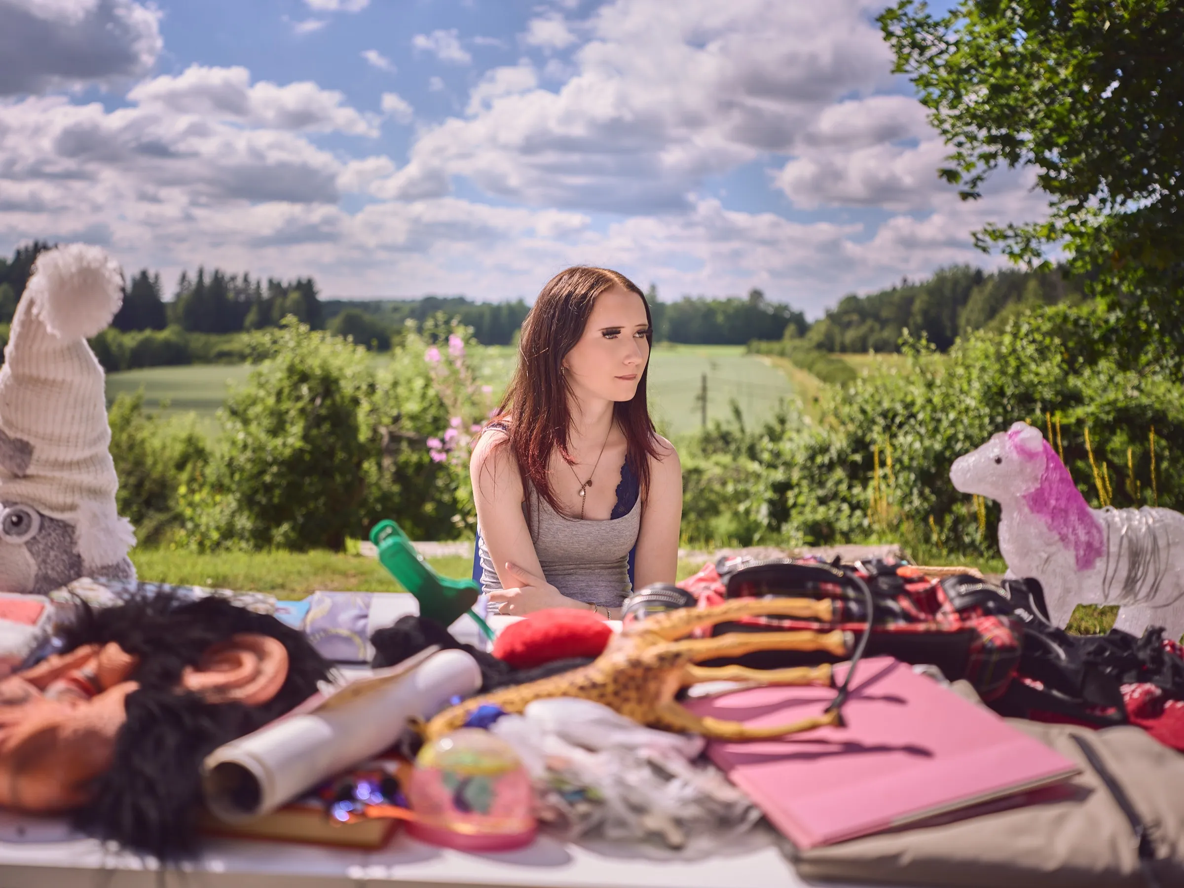 Frau hinter einem bunten Flohmarktstand, dahinter Felder und ein weiter Himmel
