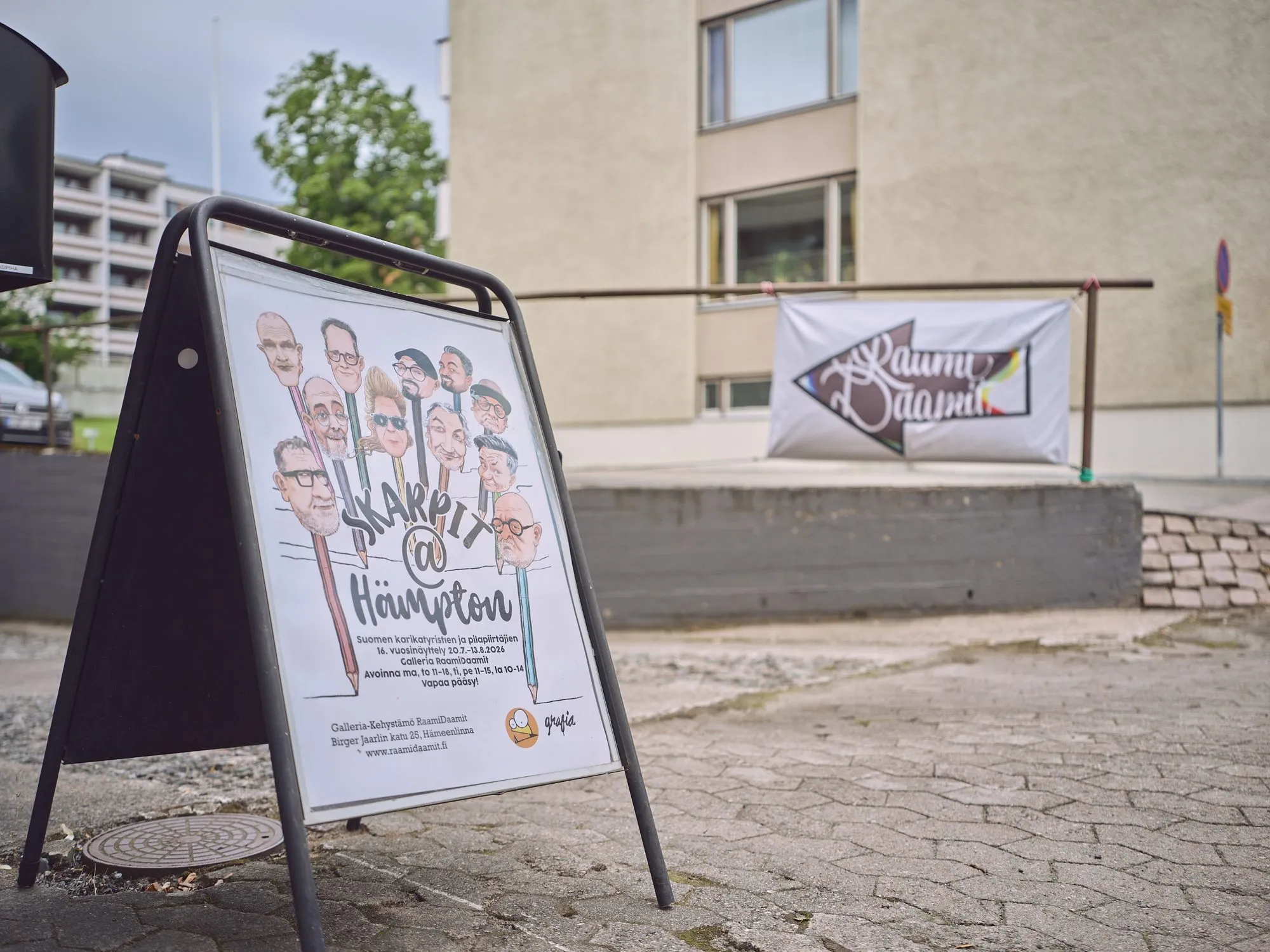 Aufsteller vor der Tür mit dem Plakat Skarpit @ Hämpton, darauf viele Karikaturgesichter