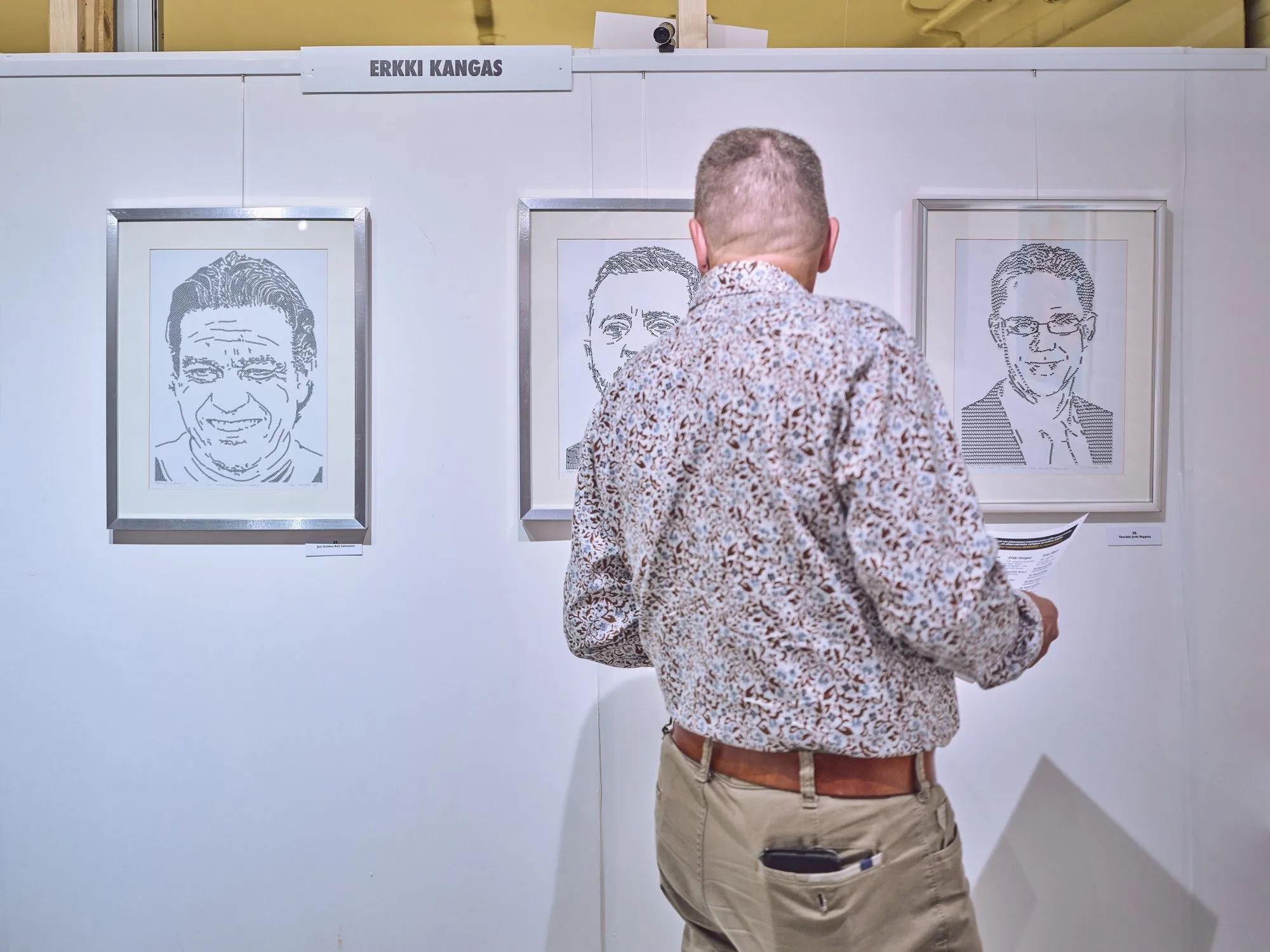 Besucher vor der Wand von Erkki Kangas mit mehreren Porträts in Schwarz und Weiß