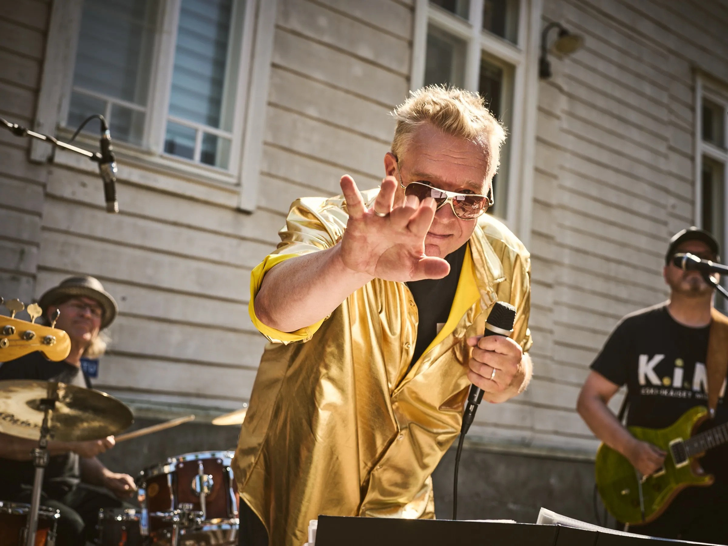 Sänger im goldenen Hemd streckt die Hand in die Kamera, Band im Gegenlicht