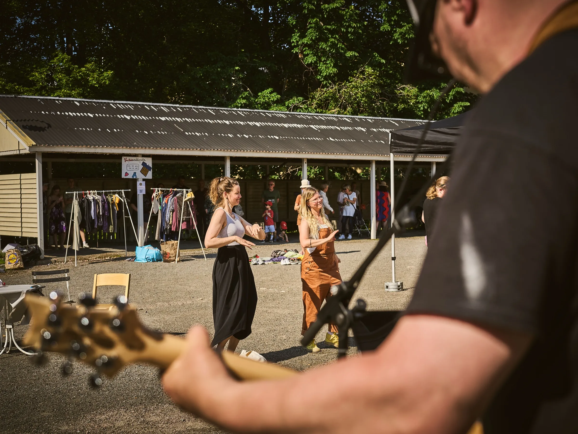 Zwei Frauen tanzen vor den Kleiderständern der Tauschstation, im Vordergrund ein Bassist