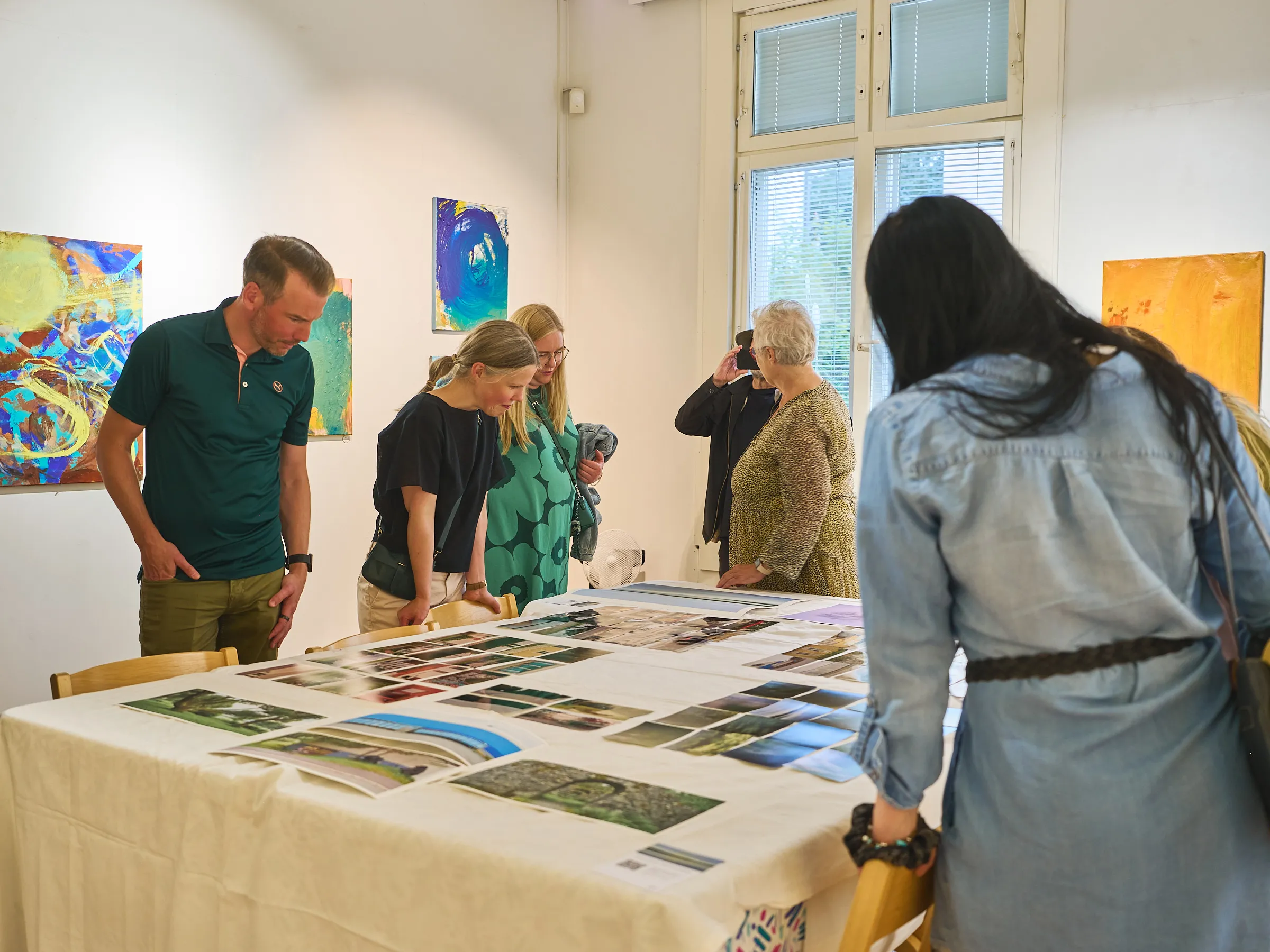 Menschen stehen um einen langen Tisch mit ausgelegten Fotografien, jemand fotografiert im Hintergrund