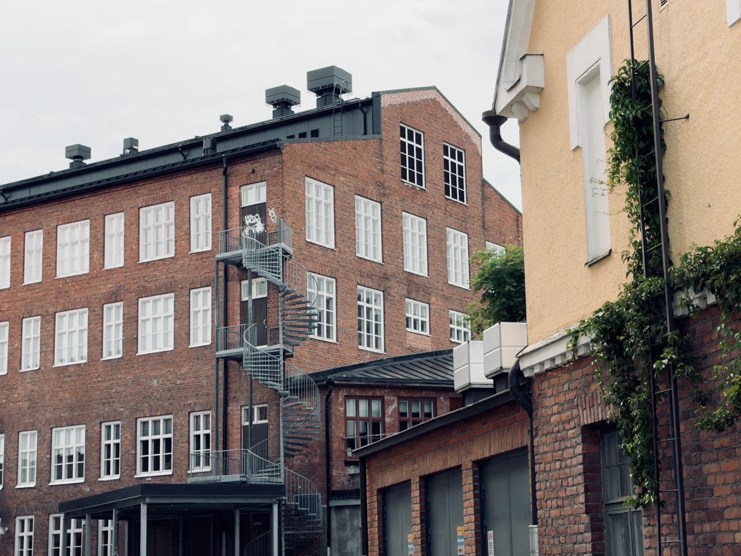 Lange rote Backsteinfassade der ehemaligen Tuchfabrik mit Wendeltreppe, rechts der gelbe Giebel