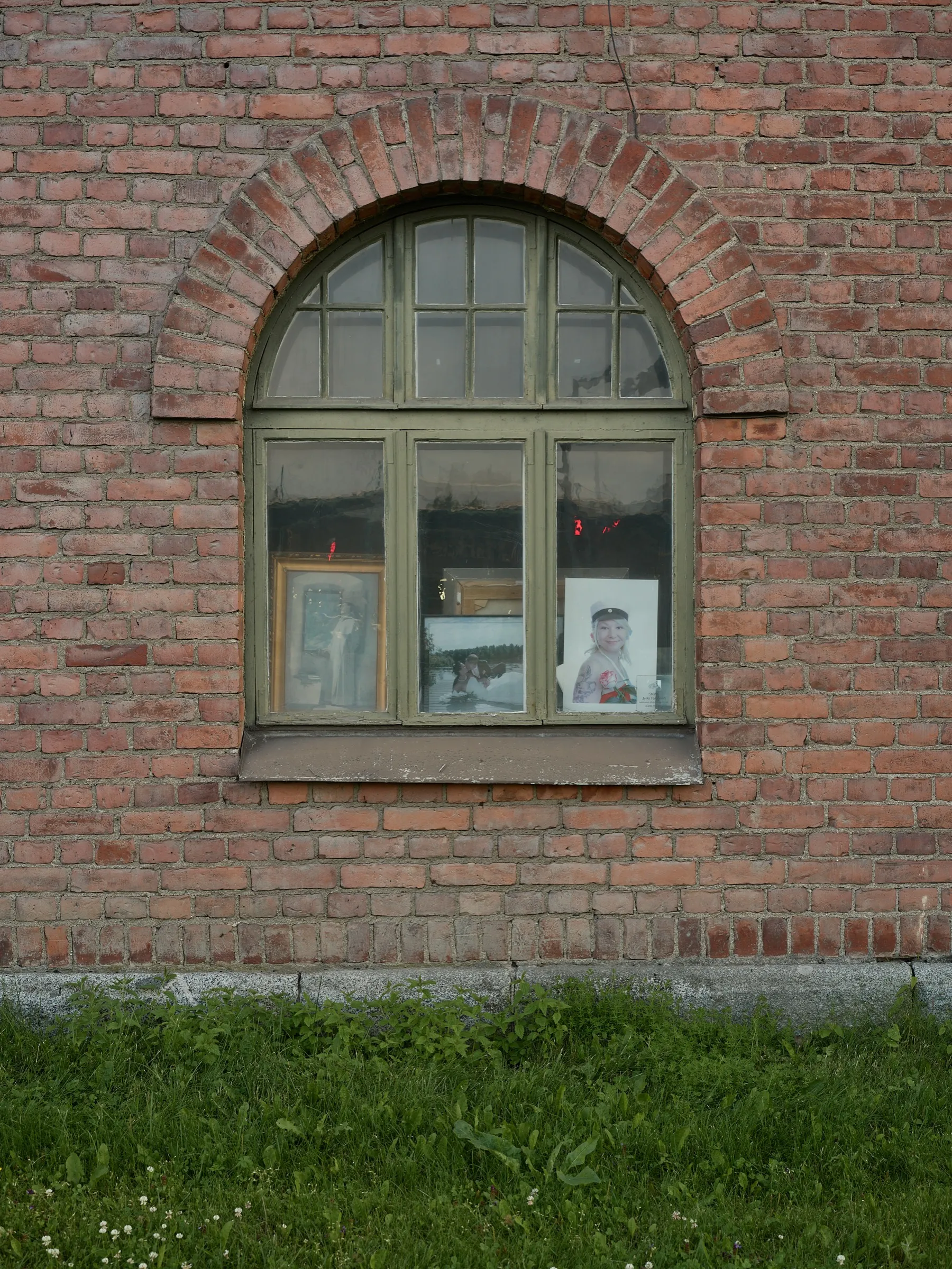 Rundbogenfenster im roten Ziegelmauerwerk, innen lehnen gerahmte Bilder