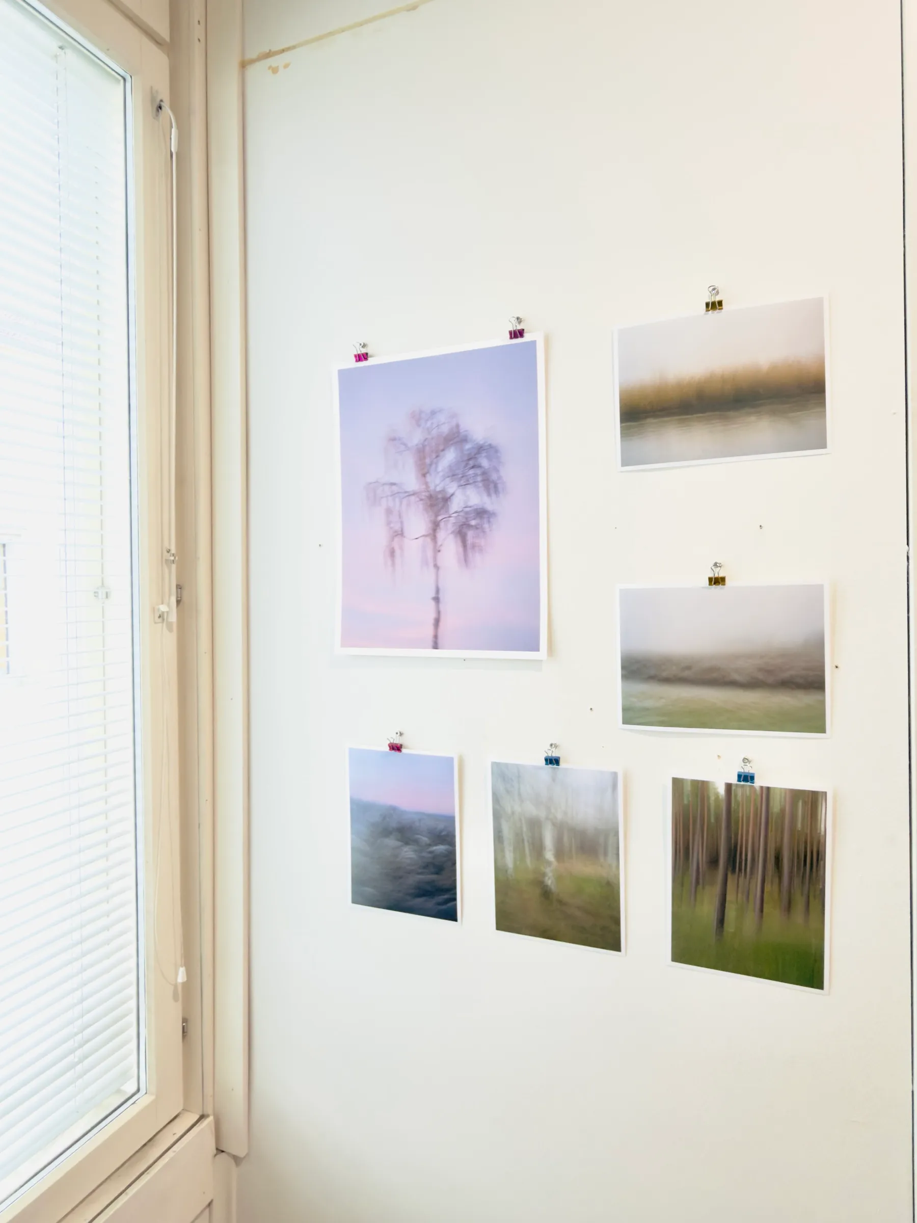 Ausgedruckte Fotoabzüge der Serie „Heimat“, mit Bürobinderklammern an eine weiße Wand geheftet