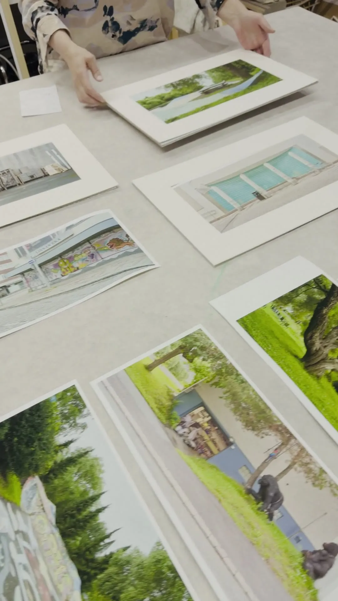 Video: Prints in Passepartouts liegen auf dem Arbeitstisch der Rahmenwerkstatt, eine Hand ordnet sie