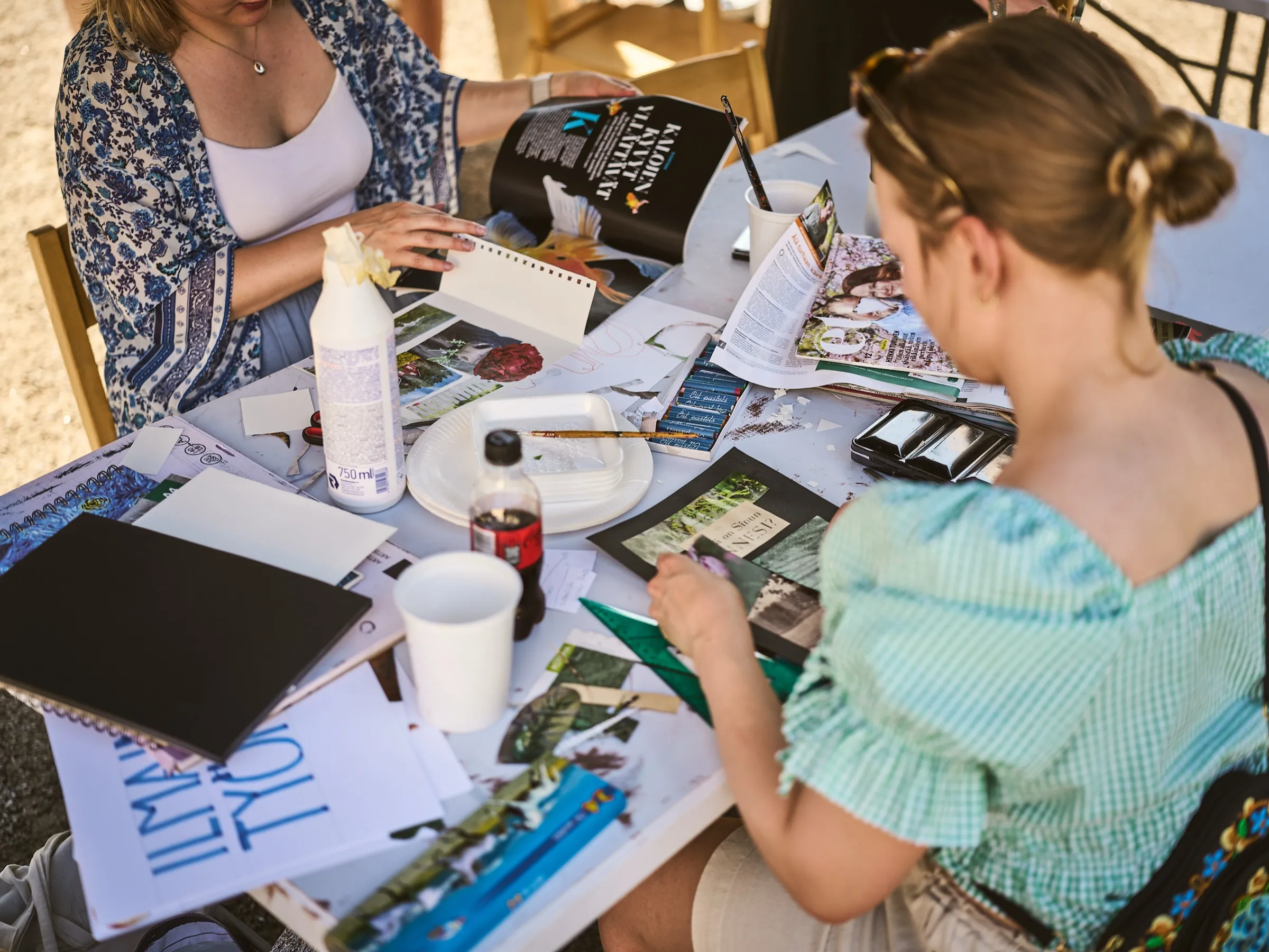 Zwei Frauen an einem Tisch mit Ölpastellen, Zeitschriften und Collagematerial